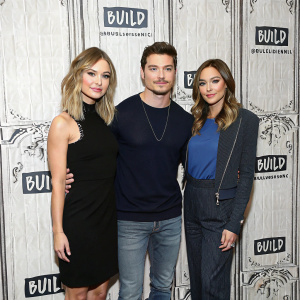 At the BUILD Series Event, Christine Evangelista, Josh Henderson, and Carrera Patterson pose for photographers. Christine in black dress, Josh in casual wear, Carrera in navy blue top. Behind them, the BUILD Series backdrop.