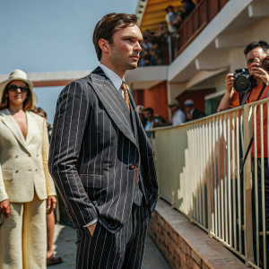 Nicholas Hoult, dressed in a dark blue suit with a subtle striped pattern and a matching tie, poses for a photo at the Cannes Film Festival. Crowded backdrop of fans and paparazzi.