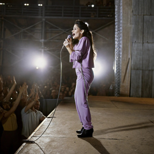 Selena Quintanilla performing live at a concert. Purple outfit, vibrant stage lights