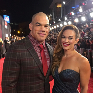 Tito Ortiz and Kristin Ortiz, a couple at a glitzy awards ceremony. Tito in a plaid shirt, crimson tie. Kristin with flowing brown hair and radiant smile. Crowded red carpet with flashing cameras