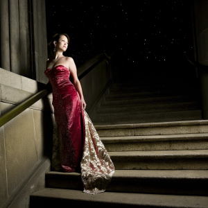Lucy Liu, at the Met Gala. Wearing an elegant red velvet dress with intricate beading and long train. Dark, starry night sky backdrop.