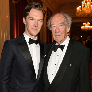 Benedict Cumberbatch and Sir Michael Gambon attending a gala. Formal attire, indoor setting with elegant decor. Warm lighting