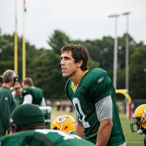 Brady Quinn, football quarterback, wearing green practice jersey with team logo, amidst a training camp setting.