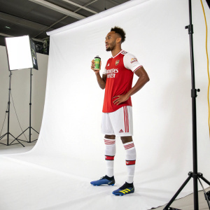 Pierre-Emerick Aubameyang, dressed in Arsenal's kit, during a promotional shoot for a sports drink brand. Behind him, a simple white backdrop