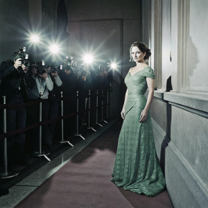 Emilia Clarke in a stunning emerald green dress at an awards show. Red carpet backdrop, paparazzi in the background