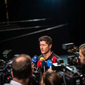 Robert Lewandowski in an interview session. Press conference with many microphones and cameras in front of him. Dark stage background