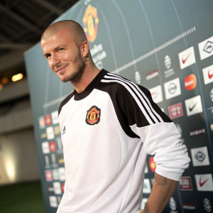 David Beckham, bald head, dressed in white and black Manchester United jersey. Posing for photo. Behind him, array of sponsors logos
