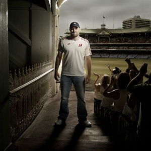 Andrew Flintoff, wearing a Vodafone branded t-shirt, baseball cap and jeans. At an outdoor cricket stadium, surrounded by fans and reporters.