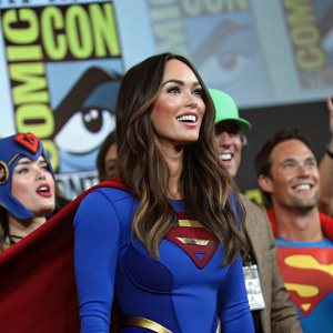 Megan Fox at Comic-Con, dressed in a blue superhero costume. Surrounded by fans and cosplayers.