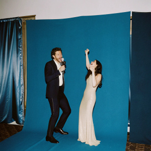 Brett Eldredge in a sleek black suit and Hailee Steinfeld in a shimmering white gown, posing excitedly on stage during the Grammy Awards ceremony.