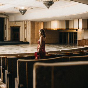 Emma Roberts in a stylish red carpet outfit. She is standing alone in a large, empty theater lobby.