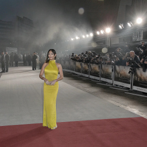 Aarti Mann at 'The Recruit' premiere, wearing a stunning bright yellow gown with a high neckline and tailored fit. Surrounded by the promotional backdrop at a bustling red carpet event.
