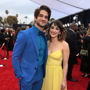 Tyler Posey, actor, and Seana Gorlick, makeup artist, at the 2023 Grammy Awards. Tyler in a blue suit, Seana in a yellow dress. Crowded red carpet.