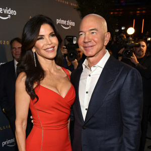 Lauren Sanchez and Jeff Bezos attend an Amazon event. Lauren in a bold red dress, Jeff in a sharp suit. Both smile for photographers amidst a sea of celebrities.