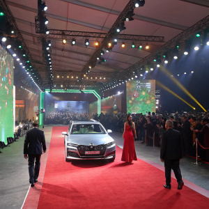 Skoda Superb unveil at auto expo. Formal attire, red carpet, large crowd, stage lights, vibrant colors