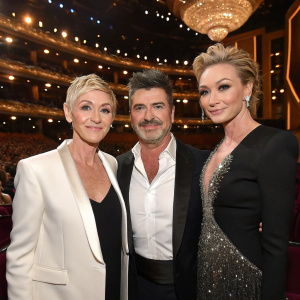 Ellen DeGeneres, Simon Cowell, and Portia de Rossi at an awards ceremony. Lavish venue with chandeliers and plush seating.