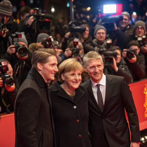 Angela Merkel, Bastian Schweinsteiger, and Soenke Wortmann attend Berlinale Film Festival. Crowded red carpet. Paparazzi flashing lights.