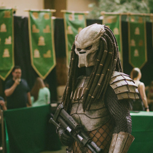 Detailed cosplay of Tina from the Alien franchise. Monsterpalooza convention backdrop with green banners featuring castles. Photographer captures candid moment.