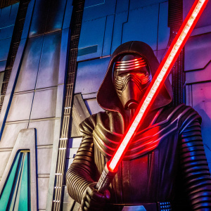 Kylo Ren from Star Wars franchise, stern expression, dark hair, rugged appearance, standing against a dark, abstract background highlighting the red glow from his lightsaber.