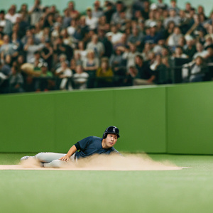 Kurt Suzuki, wearing a blue jersey, at the baseball diamond. He slides into base. Crowd cheering, blurred spectators in background.