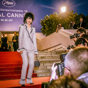Maggie Cheung at Cannes Film Festival. Wearing a classic black and white suit with matching clutch. Red carpet with flashing cameras