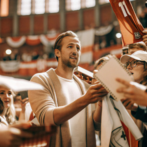 Harry Kane, in a casual outfit, at a fan signing event. Crowded and vibrant sports arena.