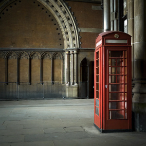 A vintage red British telephone box adorned with a golden crown emblem stands prominently outside the St Pancras Renaissance Hotel in London. Set against the backdrop of Gothic architecture, the hotel's facade boasts intricate details and a towering archway entrance.