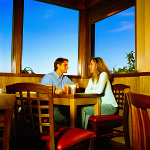 Will Estes and Vanessa Lengies, smiling at a cozy cafe. Warm lighting, wooden interiors. Will wears a light blue shirt, Vanessa has loose waves.