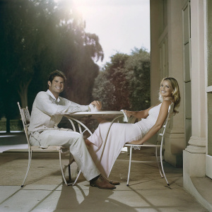 Kristin Cavallari and Matt Leinart, couple posing at an outdoor cafe. Warm sunlight, greenery in the background.