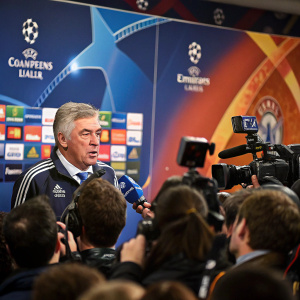 Carlo Ancelotti, the Chelsea FC manager, speaking at a packed press conference. Surrounded by journalists and camera flashes. Vibrant UEFA Champions League backdrop
