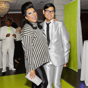 Manila Luzon and Michael J Alvarez, a charming duo, posing for a candid photo at a gala event. Manila, with her distinctive dark hair and playful demeanor, wears a striped blouse. Michael, donning glasses and a sleek suit with a tie, stands close by, with Manila playfully touching him.