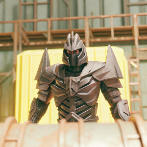 A detailed 3D model of a towering Decepticon, named Overlord, in a futuristic setting. Dark gray armor with intricate, angular designs, set against a metallic backdrop.