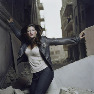Gina Carano stars in the action-packed film 'Scorched Earth.' She stands in a dramatic, powerful stance against a backdrop of ruins and destruction. Directed by Peter Howitt, set for release in February.