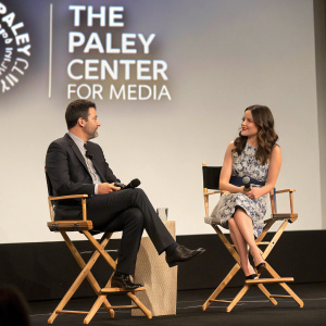 Jimmy Kimmel and Katie Lowes at The Paley Center for Media event. Both are seated on director's chairs. Behind them, the Paley Center logo stands out against a plain background.