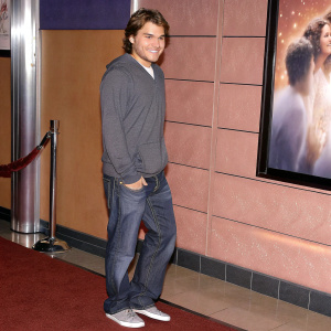 Emile Hirsch, in casual attire, at a movie premiere. Gray hoodie, jeans, sneakers. Warm smile, posing for camera. Film poster backdrop. Glamorous event, red carpet.