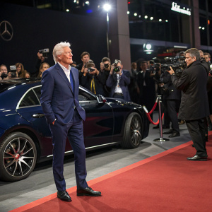 Richard Gere, in a navy blue suit, standing in front of a sleek new car model. Flashing cameras and attendees in formal wear at a glitzy auto show.