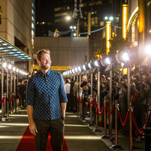 Scott Speedman, Canadian actor, smiling at the premiere. Wearing a patterned blue shirt. Crowded venue, red carpet event.