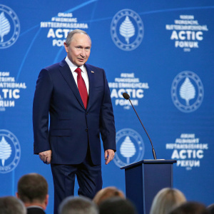 Vladimir Putin, the Russian president, in a navy suit with red tie, addresses the crowd at the International Arctic Forum. Blue backdrop with forum logo
