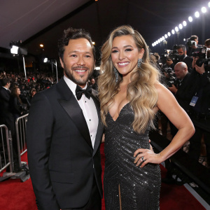 Diego Torres and Rachel Platten, elegant attire, posing at Grammy Awards ceremony. Crowded backdrop with flashing cameras