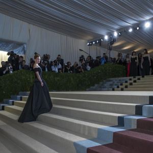 Rosie Huntington-Whiteley, stunning in a sleek black dress, struts confidently at the Met Gala. The vibrant, bustling scene with stars, paparazzi, and guests creates a lively backdrop.