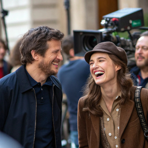 Guillaume Canet and Keira Knightley laughing on the set of a film shoot. The bustling film set in the background.