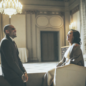 Chris Brown and Rihanna sharing a laugh during an indoor event. Decorated with chandeliers and elegant backdrops.