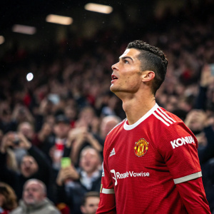Cristiano Ronaldo, intense look, wearing Manchester United jersey. Crowded stadium background, fans cheering