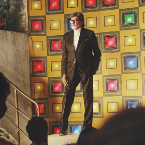 Amitabh Bachchan, the legendary Indian actor, at a Sony event. In a black suit, white shirt. Backdrop features colorful, vibrant Sony logos