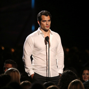 Henry Cavill, Caucasian, medium build, intense gaze, in white shirt. Center stage at a glamorous awards ceremony. Spotlight illuminates him while the audience fades into darkness.