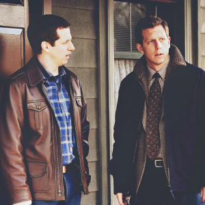Jake Peralta and Charles Boyle from Brooklyn Nine-Nine standing outside precinct, brown leather jacket over plaid shirt, dark jacket with patterned tie, building facade with window in background