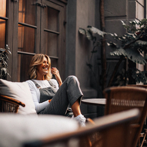 Faith Hill, joyful expression, short blonde hair, in a casual outfit, sitting on a vibrant outdoor patio with plants and wooden furniture.