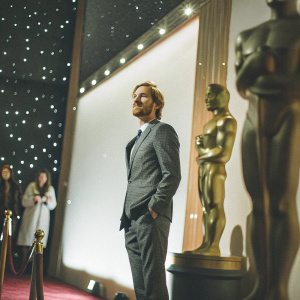 Michael Fassbender at an awards show. Wearing a dark grey suit, light stubble, short haircut. Starry night sky backdrop with award statue