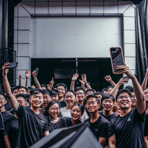 A vibrant group photo at the GOTEC LAND grand opening. Diverse Asian crowd, wearing event-branded t-shirts, against a backdrop showcasing sleek modern design and the company logo.