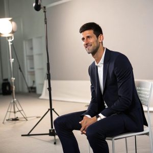 Novak Djokovic, tennis champion, in a formal suit, posing for interview. Studio setting, minimalist background.